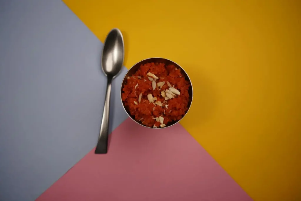 Orange suji Halwa served in a bowl alongside a spoon