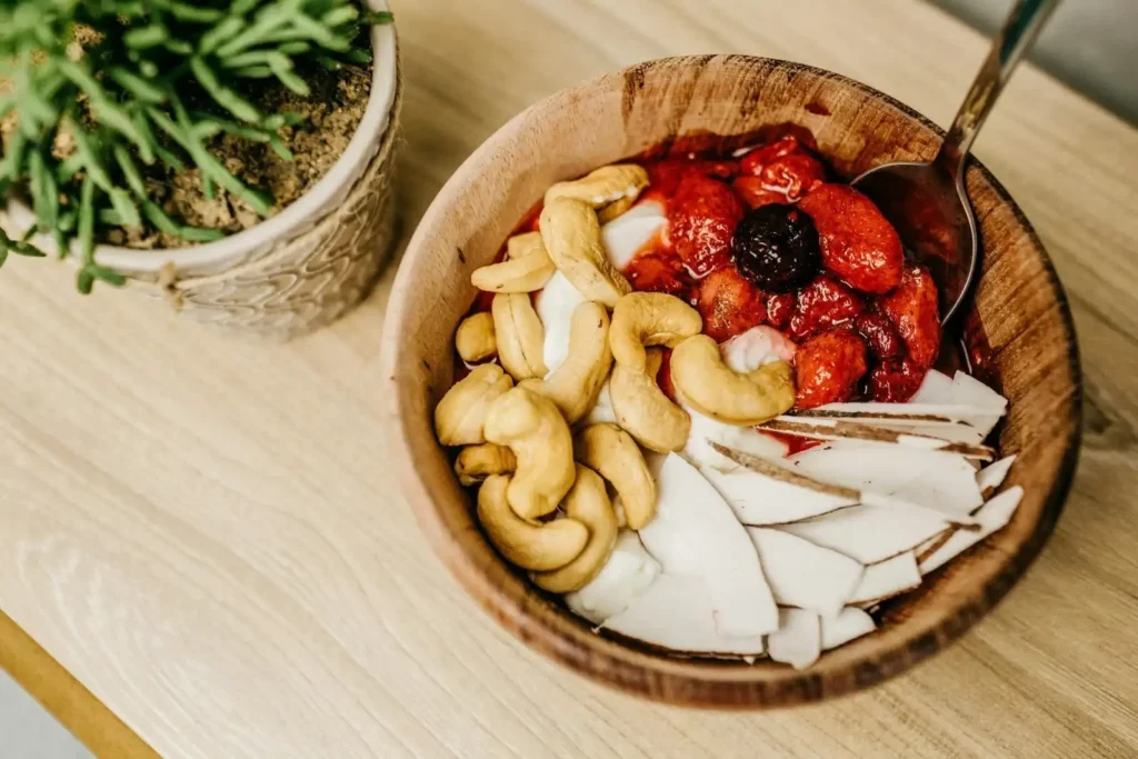 A breakfast bowl with strawberries, cream, Goan cashew nuts and coconut slices.