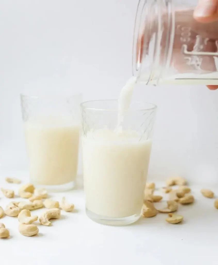 A person pouring Goan cashew nut milk in a glass.